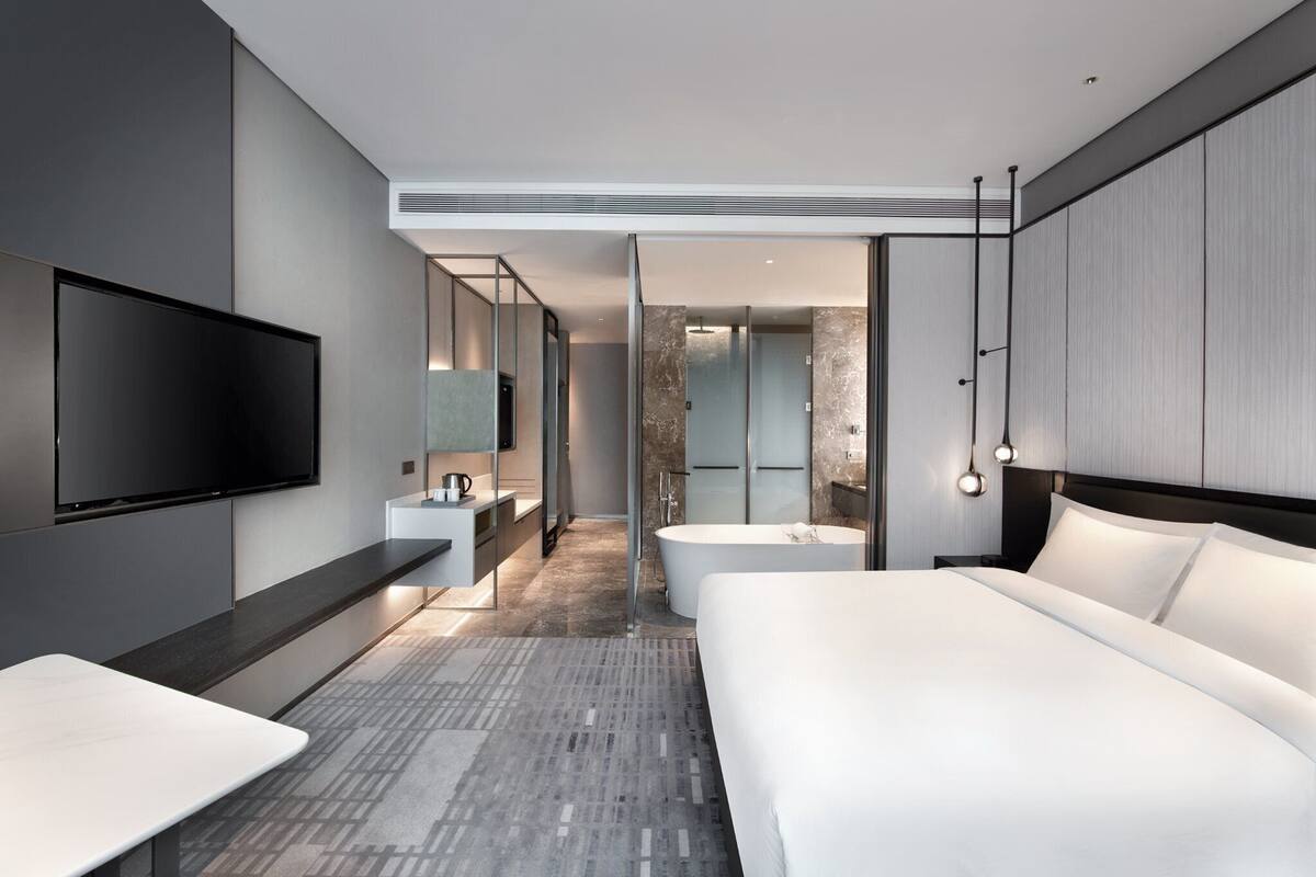 A modern hotel room with a large bed, a flat-screen TV, a desk, and a bathroom with a bathtub and shower.