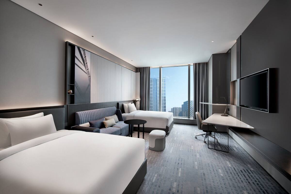 Quarto de hotel moderno com uma cama grande, um sofá, uma escrivaninha e uma televisão.