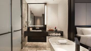 A modern bathroom with a marble floor, a black vanity with a mirror, and a white bathtub.
