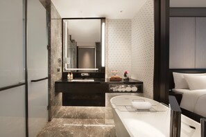 Une salle de bain moderne avec un sol en marbre, un meuble-lavabo noir doté d’un miroir et une baignoire blanche.