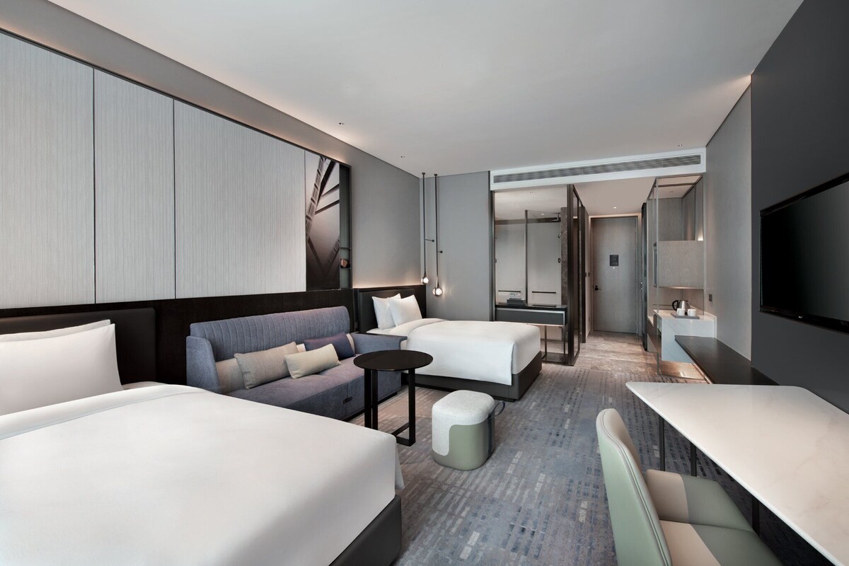 A modern hotel room with two beds, a sofa, a small table, and a TV.