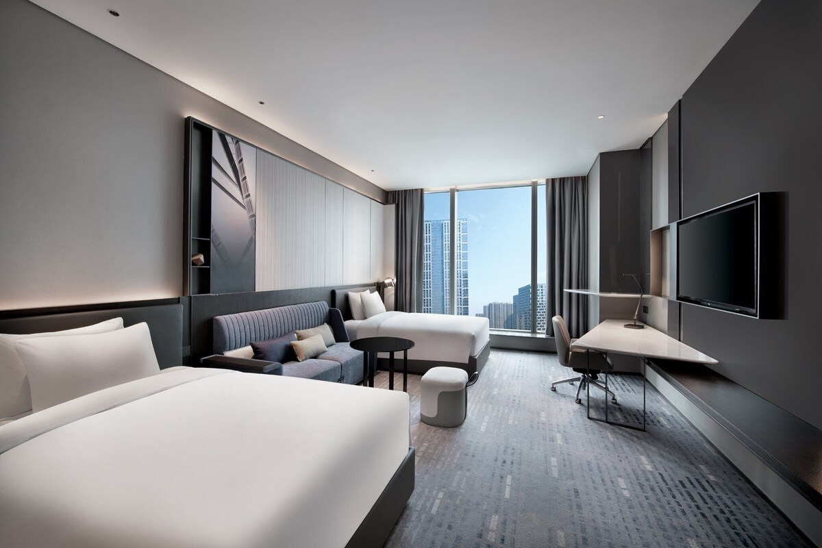 A modern hotel room with a large bed, a sofa, a desk, and a TV.