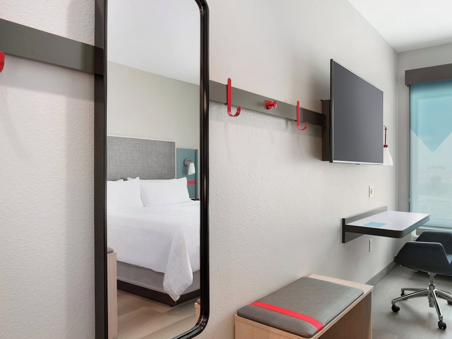 A hotel room with a bed, a desk, a chair, a TV, and a mirror.