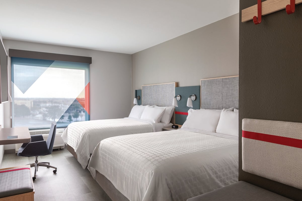 A hotel room with two beds, a desk, and a chair.