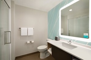 Ein modernes Badezimmer mit Duschkabine aus Glas, Toilette in Weiß, Waschbecken inklusive Spiegel und Handtuchhalter.