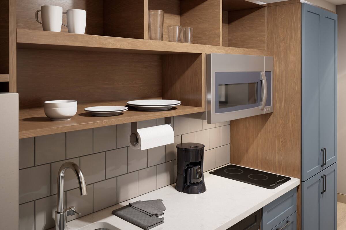 Een moderne keuken met een ingebouwde magnetron, een koffiezetapparaat en een rol keukentouwen op het aanrecht.