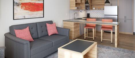 Una sala de estar moderna con un sofá gris, una mesa de centro de madera y una zona de cocina con armarios de madera y una isla central.