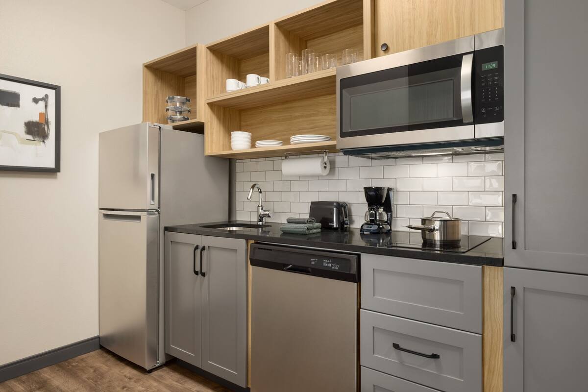 Een moderne keuken met roestvrijstalen apparatuur, houten planken en een betegelde spatwand.