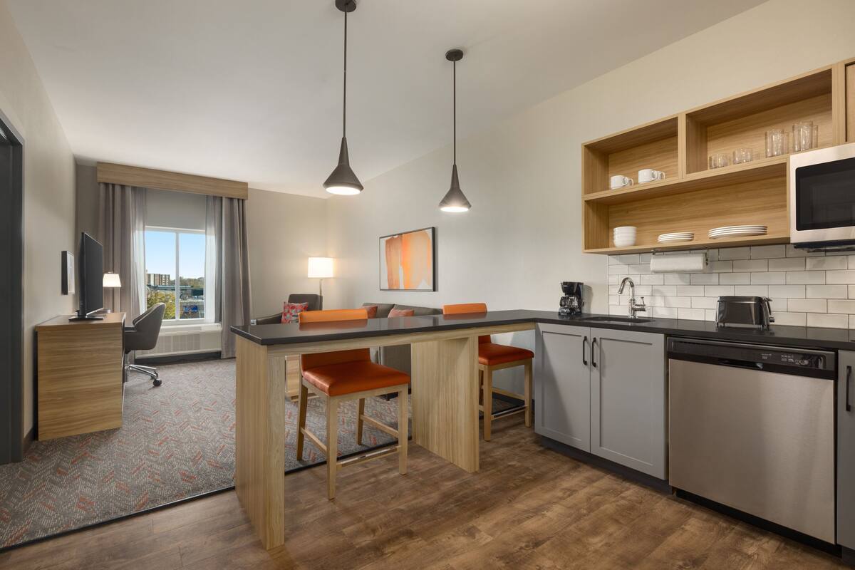 Een moderne keuken met een centraal eiland, barkrukken, een magnetron en een vaatwasser.