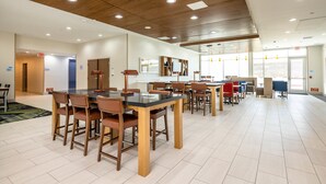 Une salle à manger spacieuse, dotée de tables et de chaises en bois, d’un plafond haut avec des luminaires encastrés et de panneaux de signalisation clairs indiquant les sorties.