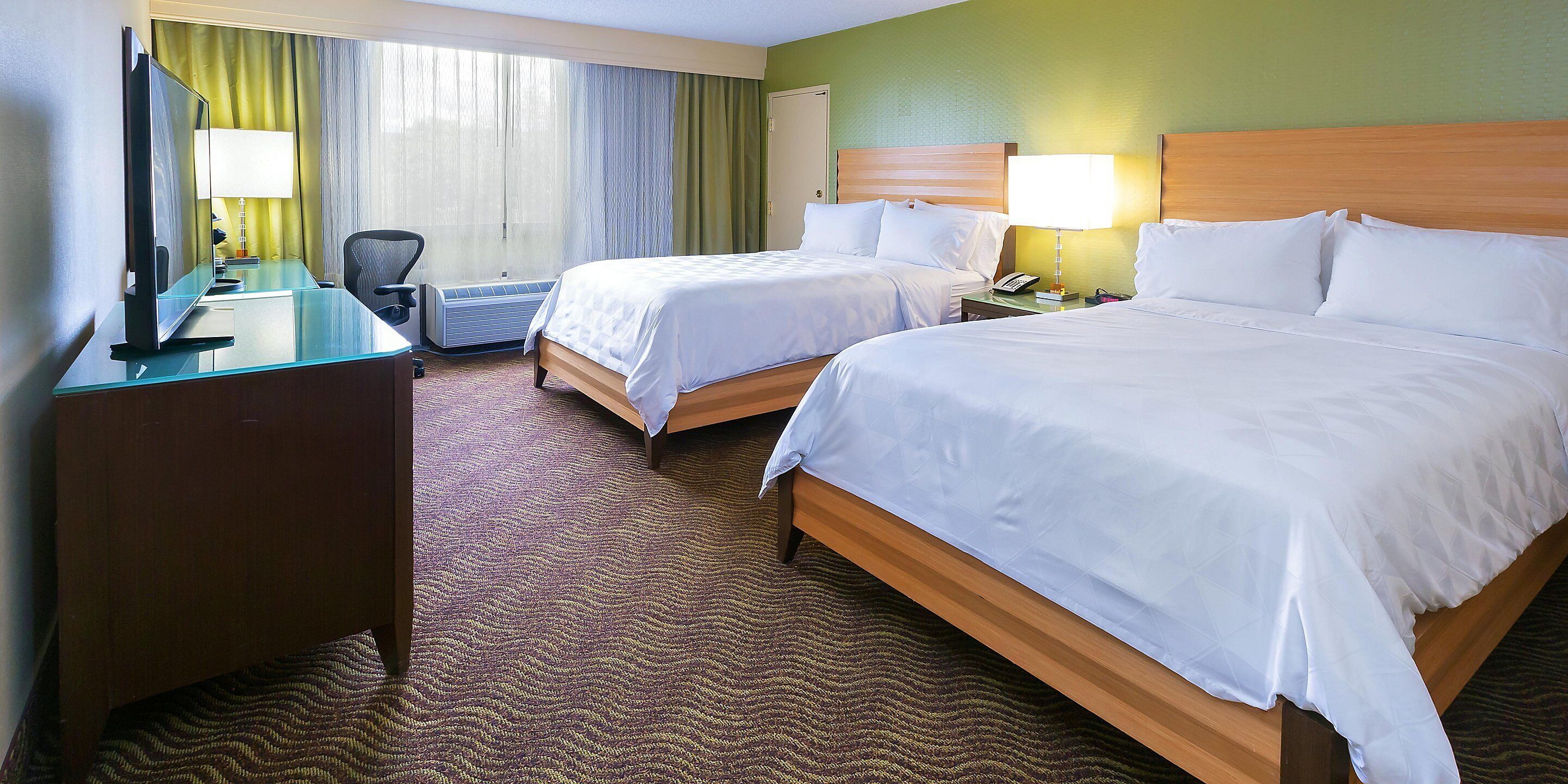 A hotel room with two beds, a desk, a chair, a TV, and a window with curtains.