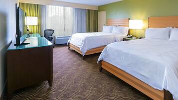 A hotel room with two beds, a desk, a chair, a TV, and a window with curtains.