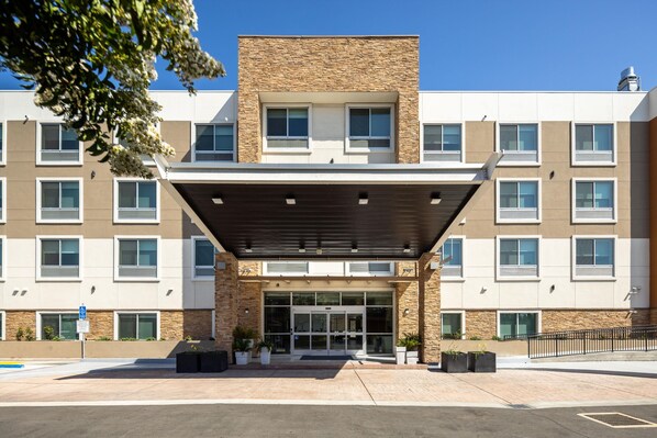 A modern building with a covered entrance, multiple windows, and a stone facade. - Holiday Inn Express & Suites San Jose Silicon Valley by IHG (San Jose)