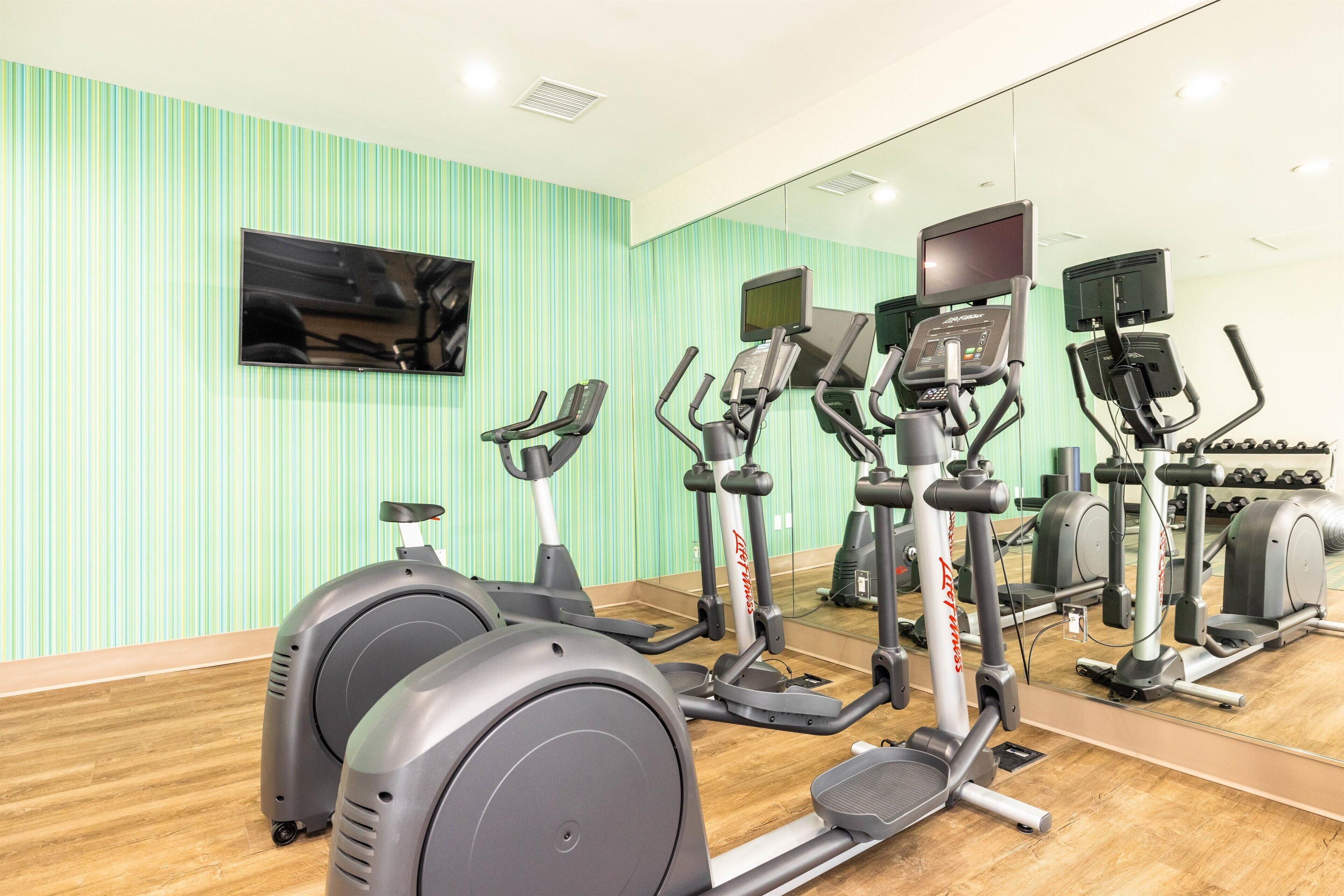 A gym with stationary bikes, treadmills, and a TV screen.