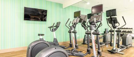 A gym with stationary bikes, treadmills, and a TV screen.
