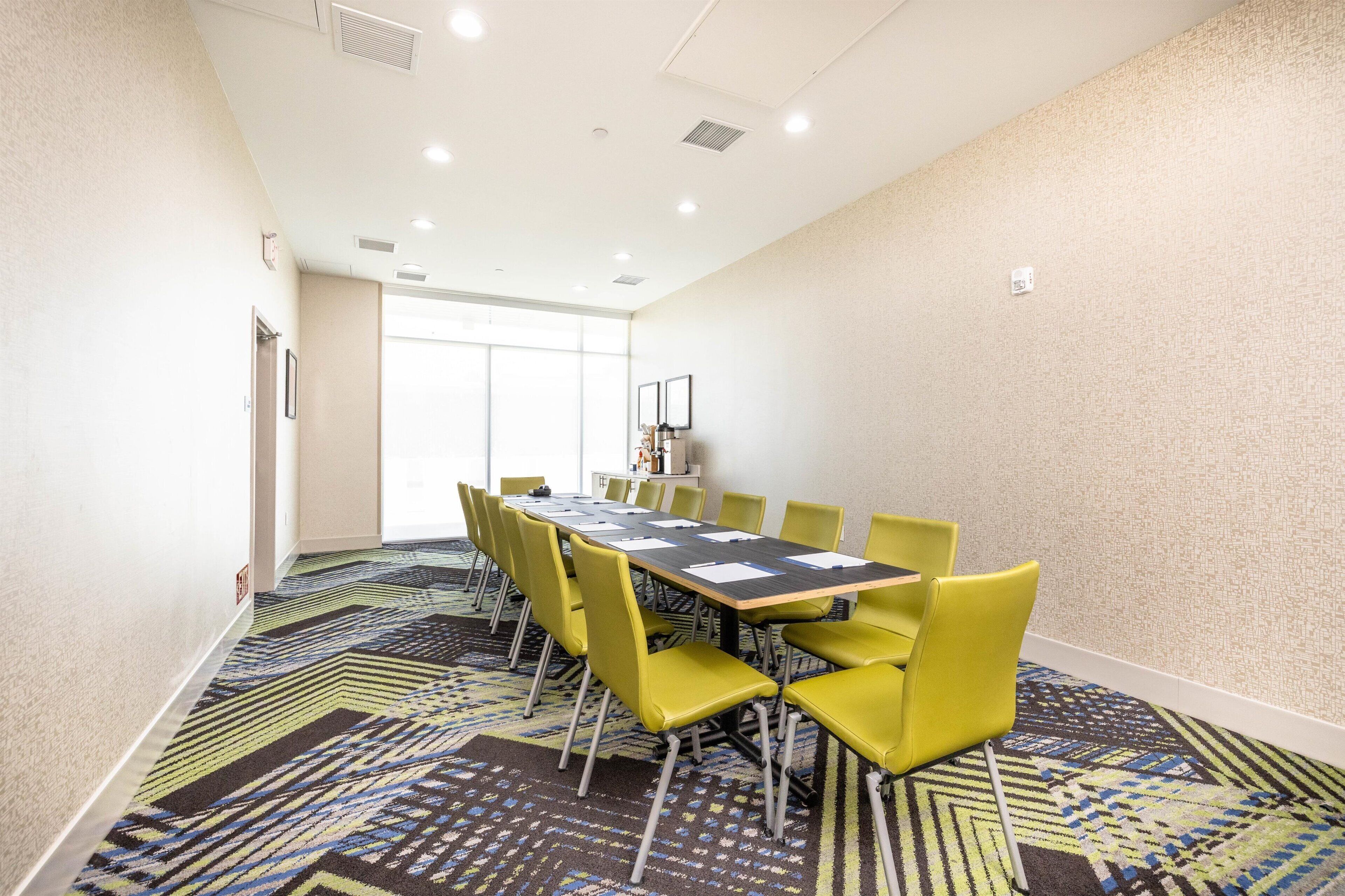 A conference room with a long table, yellow chairs, patterned carpet, and a large window.
