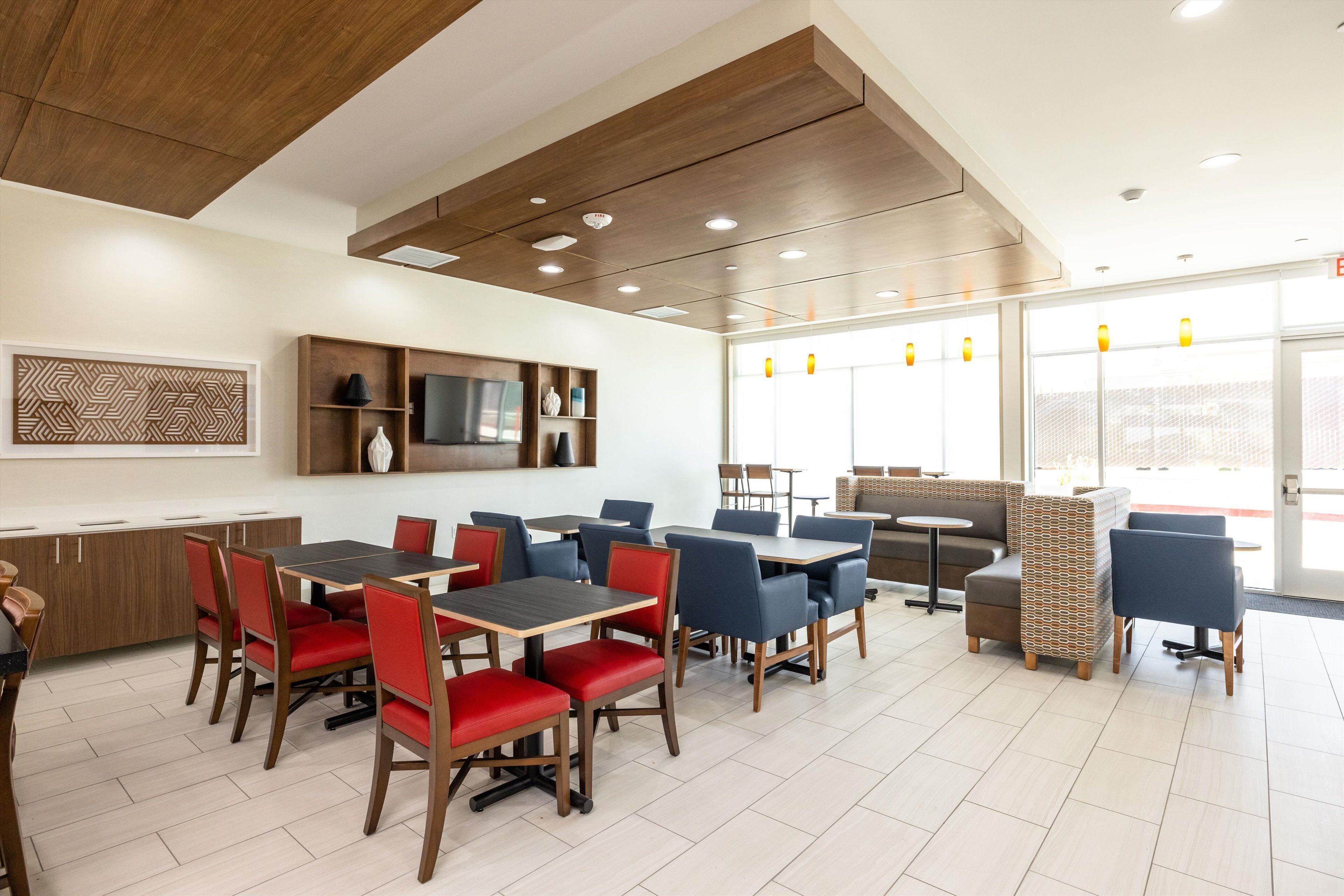 A modern dining area with wooden tables and chairs, a television, and a patterned wall decoration.