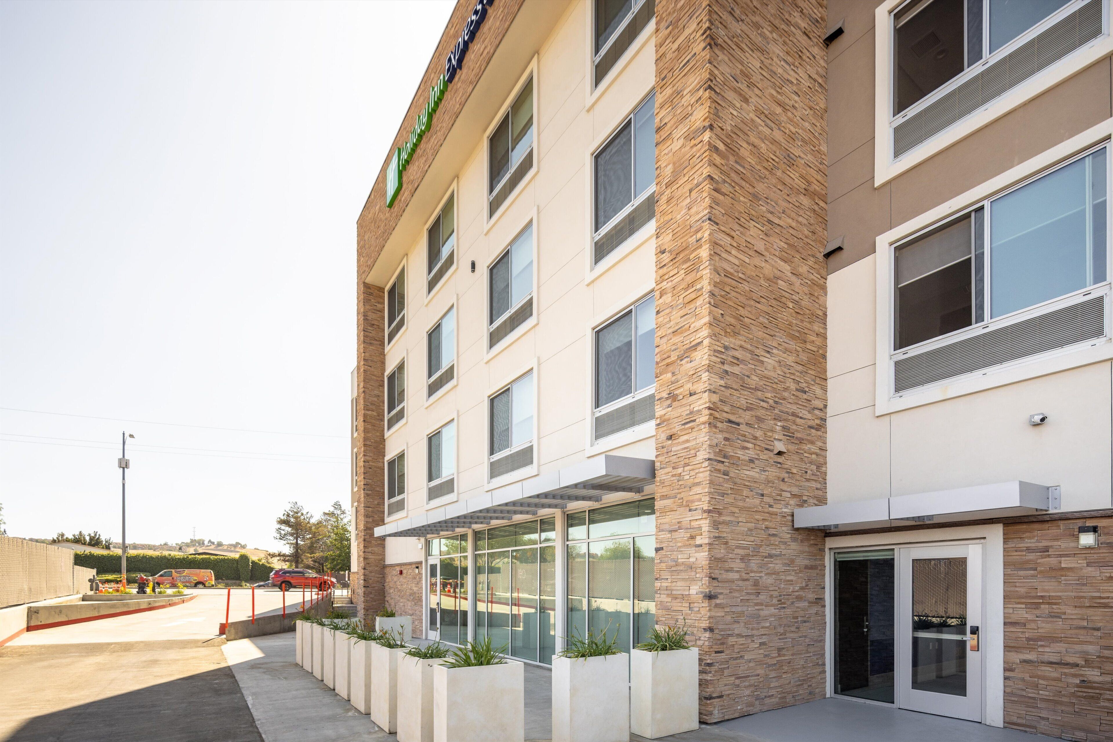 A modern hotel with a brick facade, large windows, and a covered entrance area with planters.