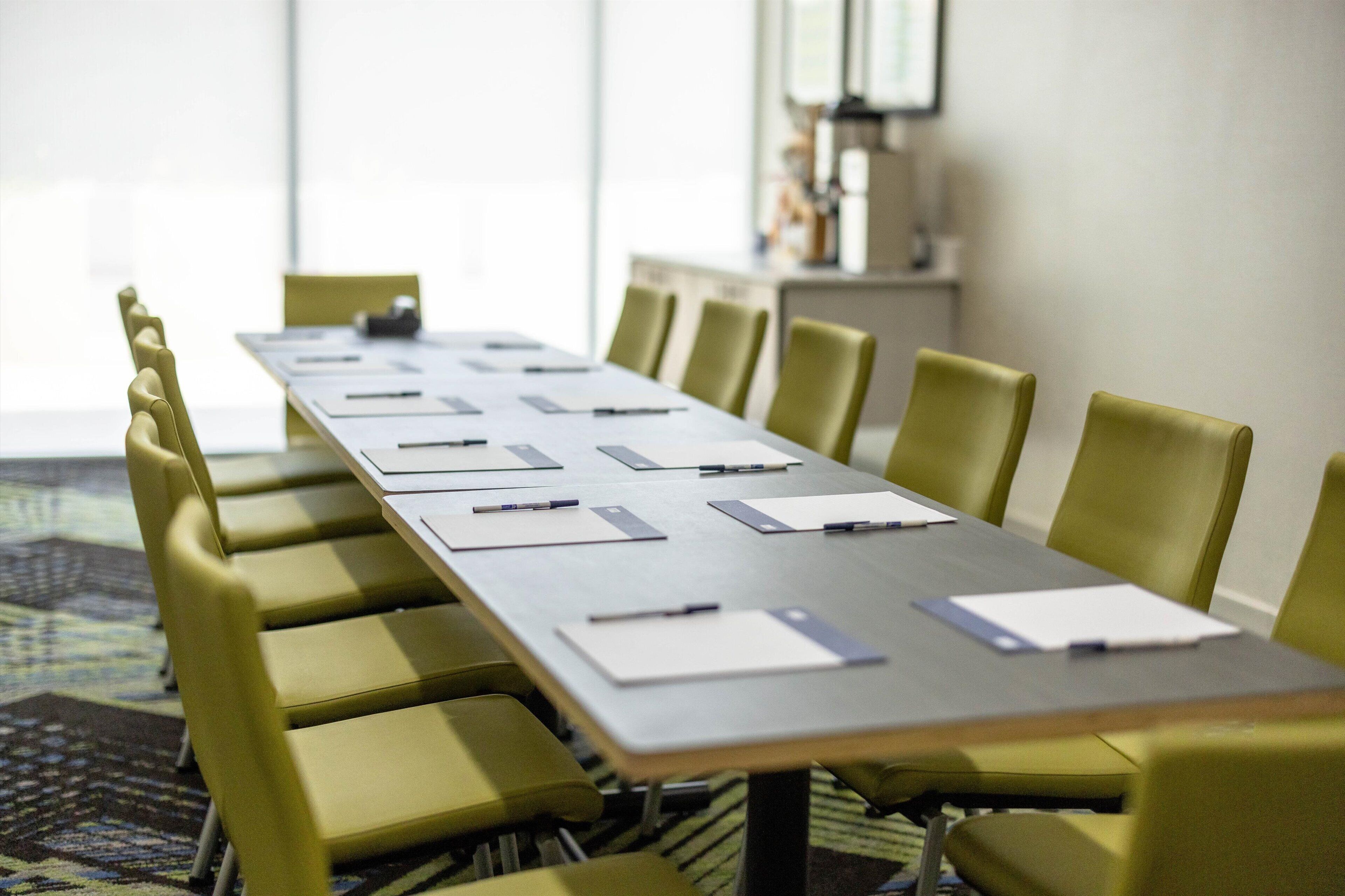 A conference room with a long table, yellow chairs, and documents on the table.