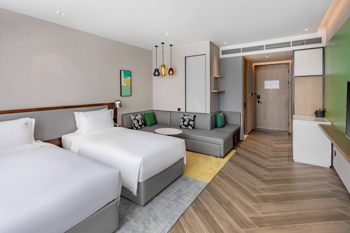 A hotel room with two beds, a sofa, a desk, and a mirror.