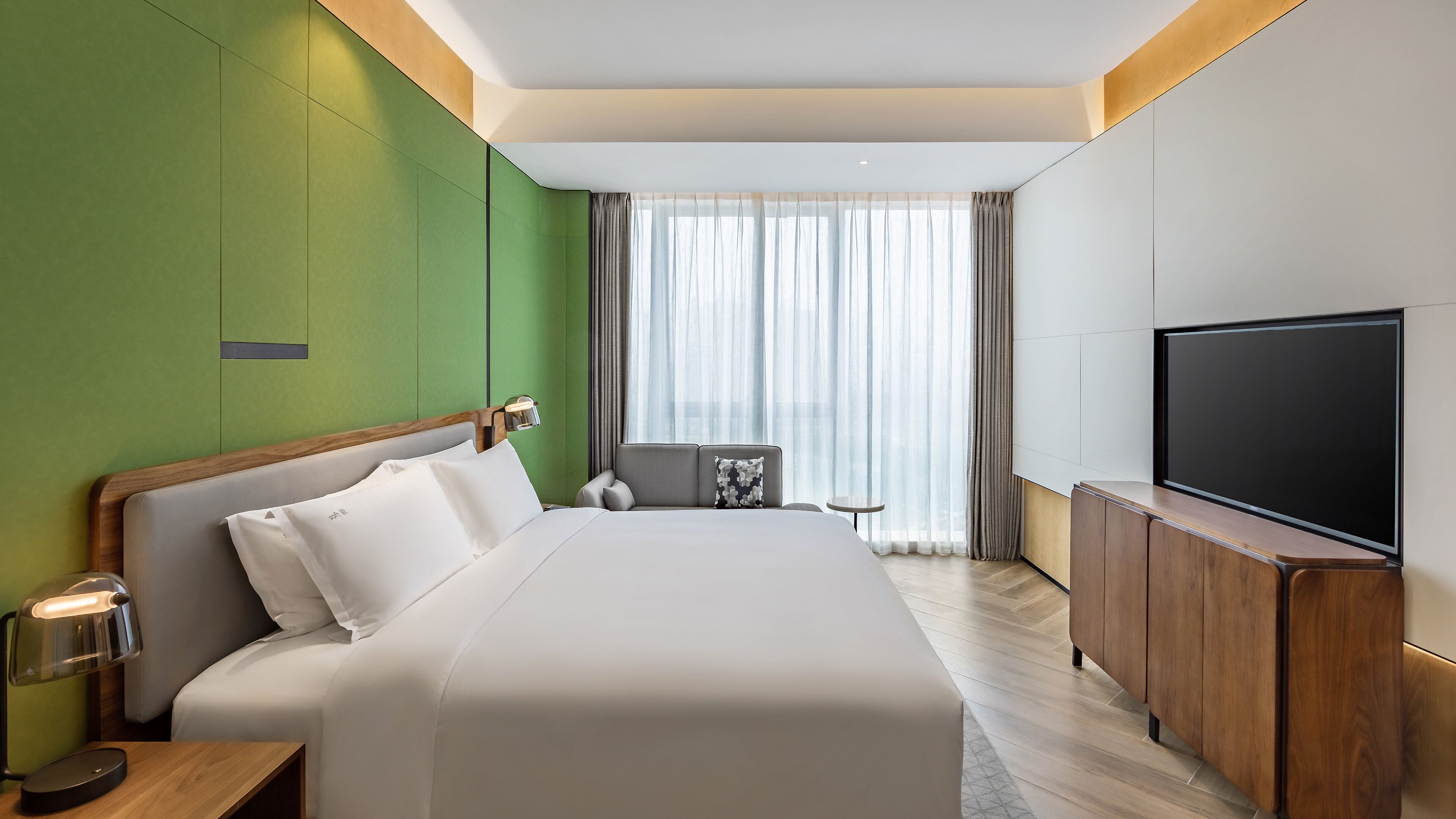 Ein modernes Hotelzimmer mit einem großen Bett, einem Fernseher und einer kleinen Sitzecke.