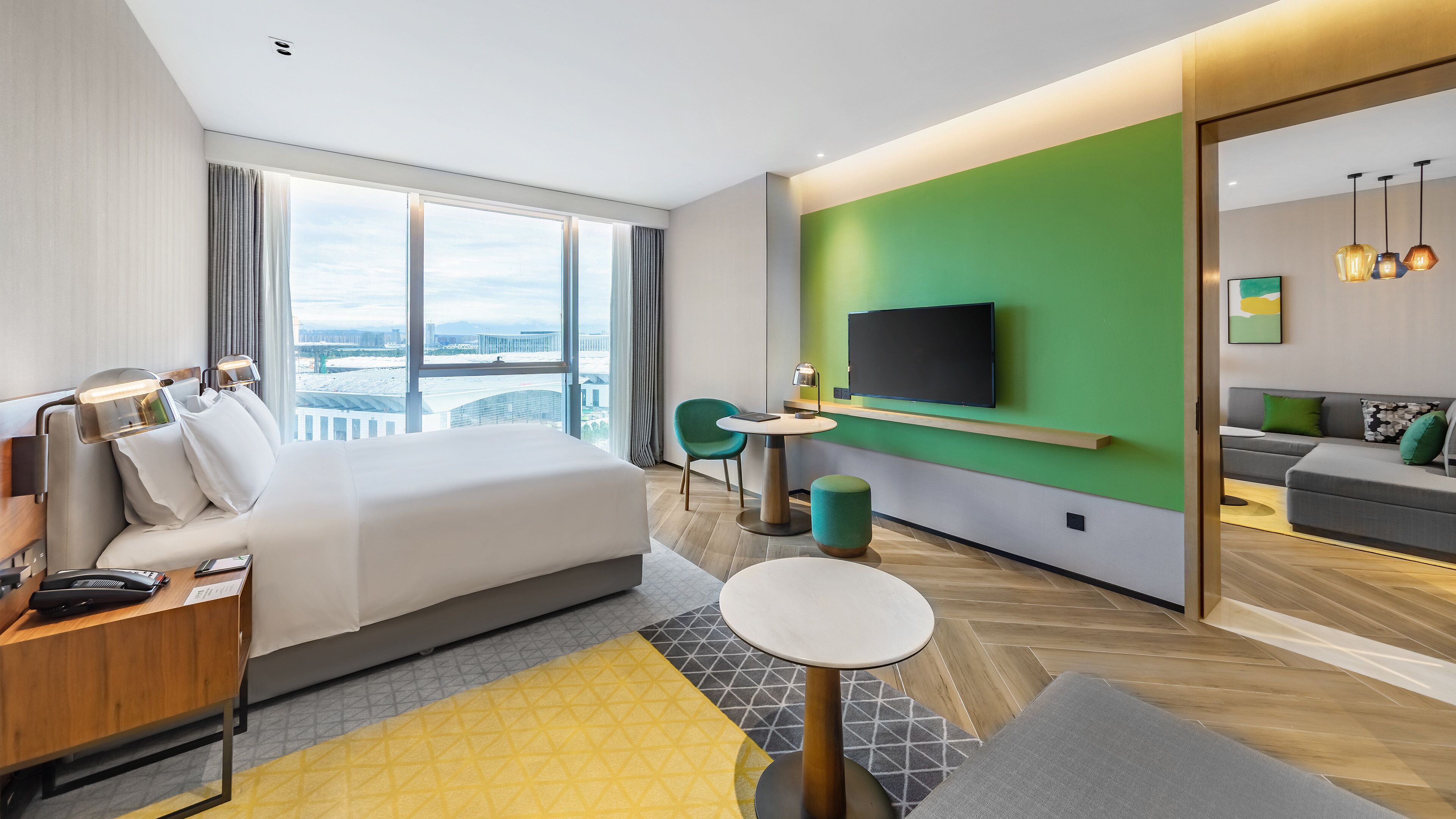 A hotel room with a bed, a desk, a TV, a sofa, and a view of the city.