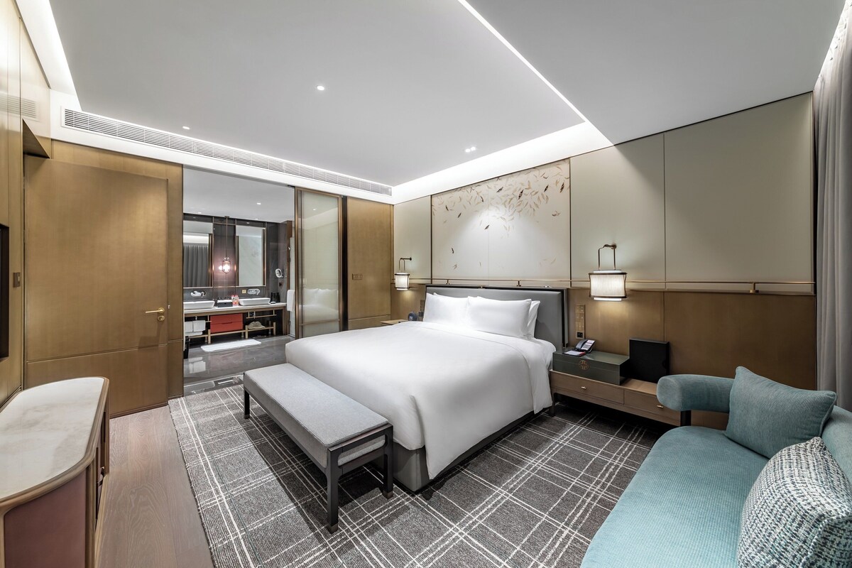 A modern hotel room with a large bed, a bench, a sofa, a desk, and a mirror.