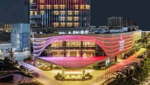 Ein modernes Hotel mit geschwungener Fassade, mehreren Etagen und einem Parkplatz.