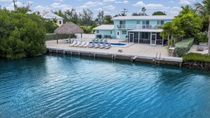 A waterfront property with a swimming pool, lounge chairs, and a thatched-roof structure. - Waterfront Private Home-7 BR, 6 Full BA, Pool, 80' Dock, Parking, Screened Porch (Marathon)