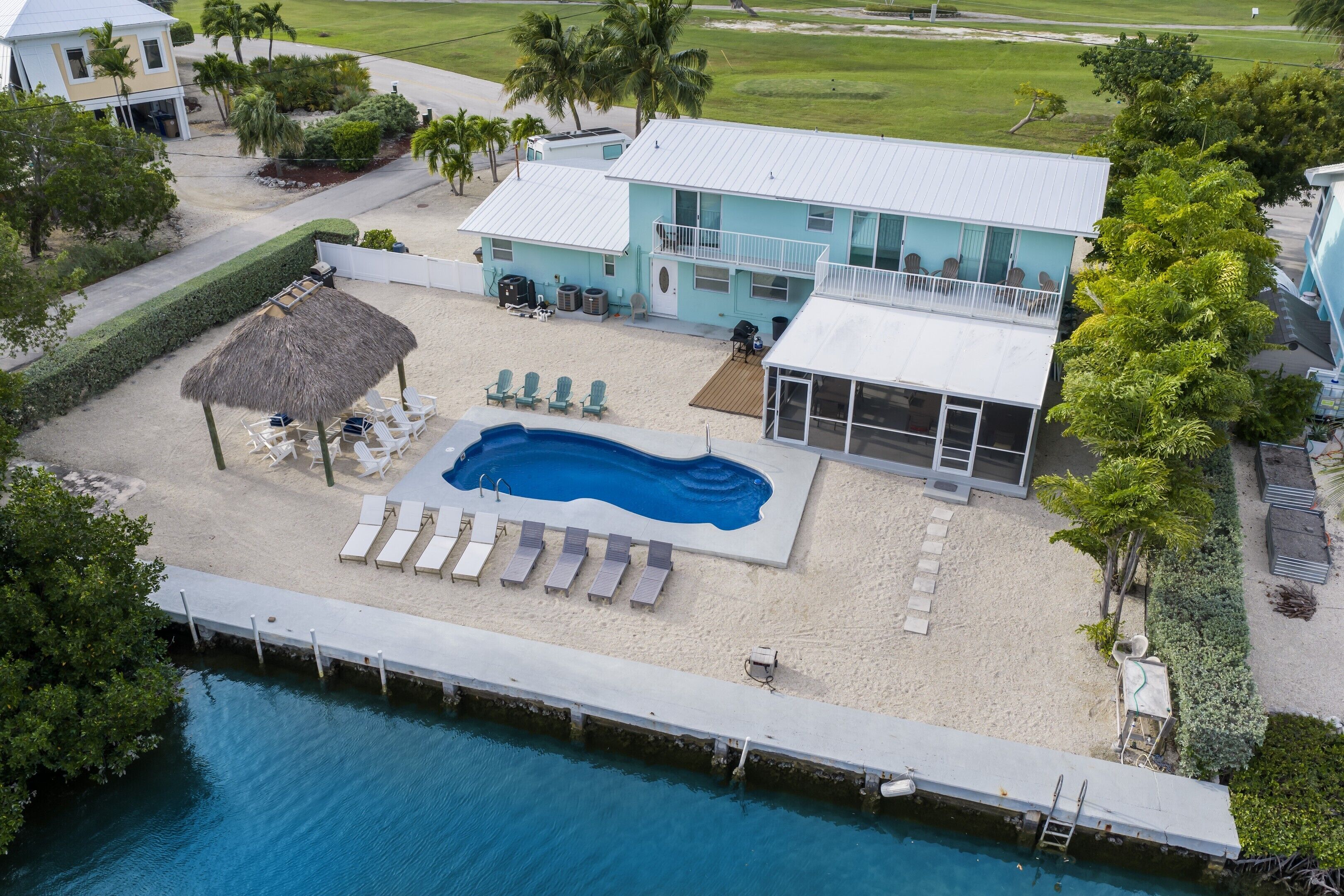 An aerial view of a beachfront property with a swimming pool, lounge chairs, and a thatched-roof structure.