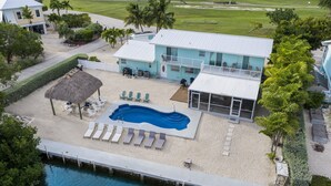 An aerial view of a beachfront property with a swimming pool, lounge chairs, and a thatched-roof structure. - Waterfront Private Home-7 BR, 6 Full BA, Pool, 80' Dock, Parking, Screened Porch (Marathon)