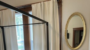 Een hemelbed met een baldakijn, een nachtkastje met een lamp en een vaas, en een spiegel aan de muur.
