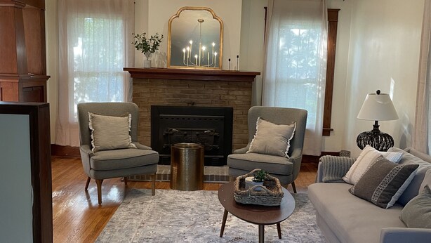 Een woonkamer met een open haard, twee fauteuils, een bank, een salontafel en een kroonluchter.