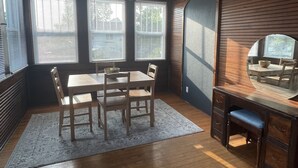 Een kamer met een houten plafond, een eettafel met stoelen, een bureau met een stoel en grote ramen met zonwering.