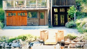 A wooden cabin with a balcony, a garage, and a dock with chairs.