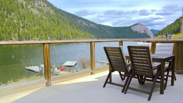 A terrace with a table and chairs overlooking a lake and forested mountains.