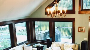 A living room with a high ceiling, large windows, a chandelier, a sofa, a coffee table, and a wooden floor.