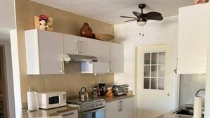 Een moderne keuken met witte kasten, een magnetron, een oven en een plafondventilator.