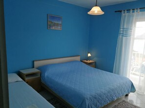 Una camera da letto con un letto blu, un comodino con una lampada, un altro comodino e un quadro appeso al muro.