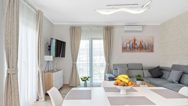 Ein modernes Wohnzimmer mit Esstisch, Sofa und einem an der Wand befestigten Fernseher.