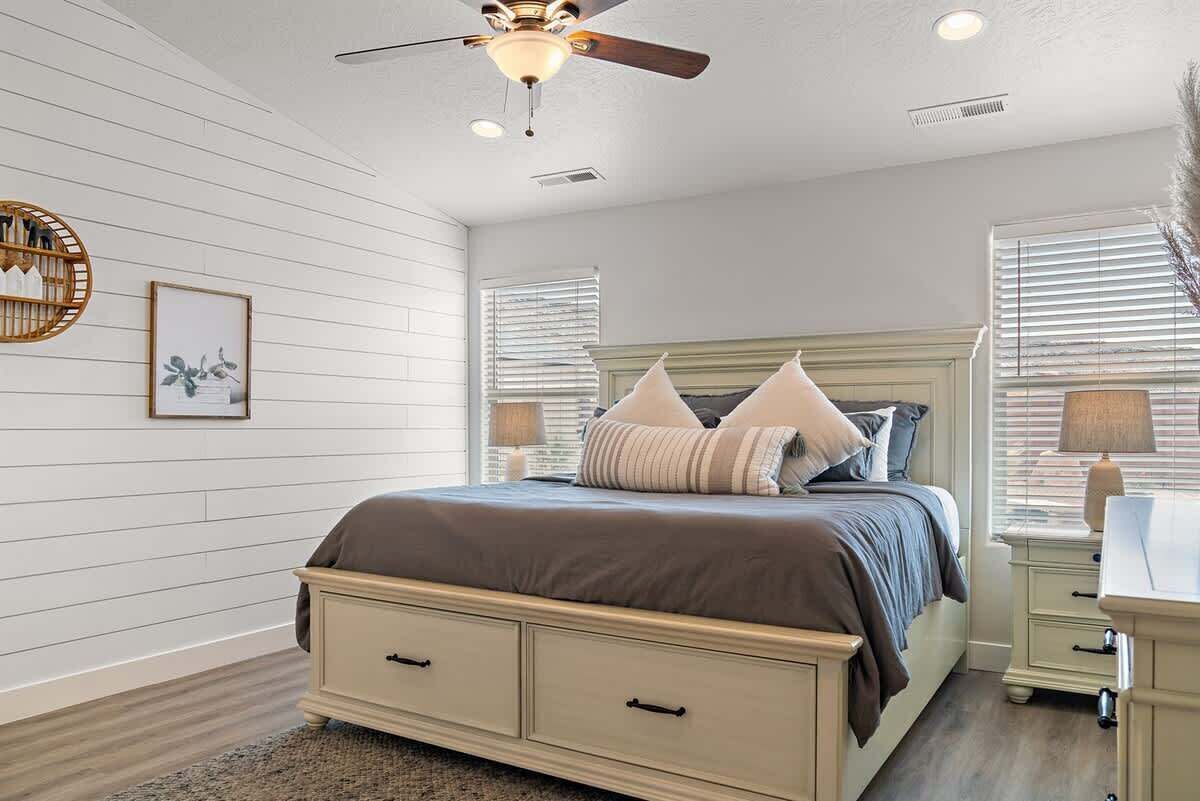 A bedroom with a bed, nightstands, a ceiling fan, and a window with blinds.