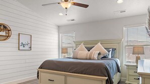 Ein Schlafzimmer mit Bett, Nachttischen, Deckenventilator und einem Fenster mit Jalousien.