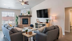 Ein Wohnzimmer mit Kamin, Flachbildfernseher, Deckenventilator und großem Fenster.