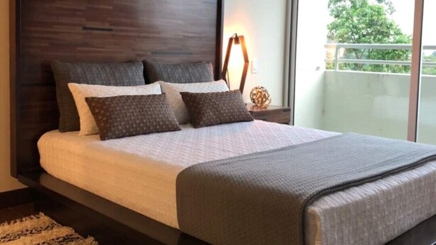 Een moderne slaapkamer met een groot bed, een donker hoofdeinde en uitzicht op een balkon.