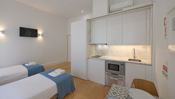 Une chambre d’hôtel compacte comprenant deux lits simples, une petite kitchenette, un téléviseur fixé au mur et un coin repas avec une table et des chaises.
