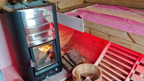 A wood-burning stove with a glass door, a wooden log storage area, and a red mat on the floor. - Ferienhaus in See Nähe! Ruhige Lage. Wlan, Bettwäsche und Handtücher Inkl (Klein Sien)