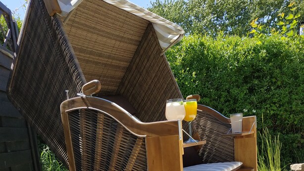 A wooden outdoor seating area with a bench and a table, surrounded by greenery and a sandy ground. - Ferienhaus in See Nähe! Ruhige Lage. Wlan, Bettwäsche und Handtücher Inkl (Klein Sien)