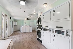A laundry room with multiple washing machines, a drying rack, and a ceiling fan.