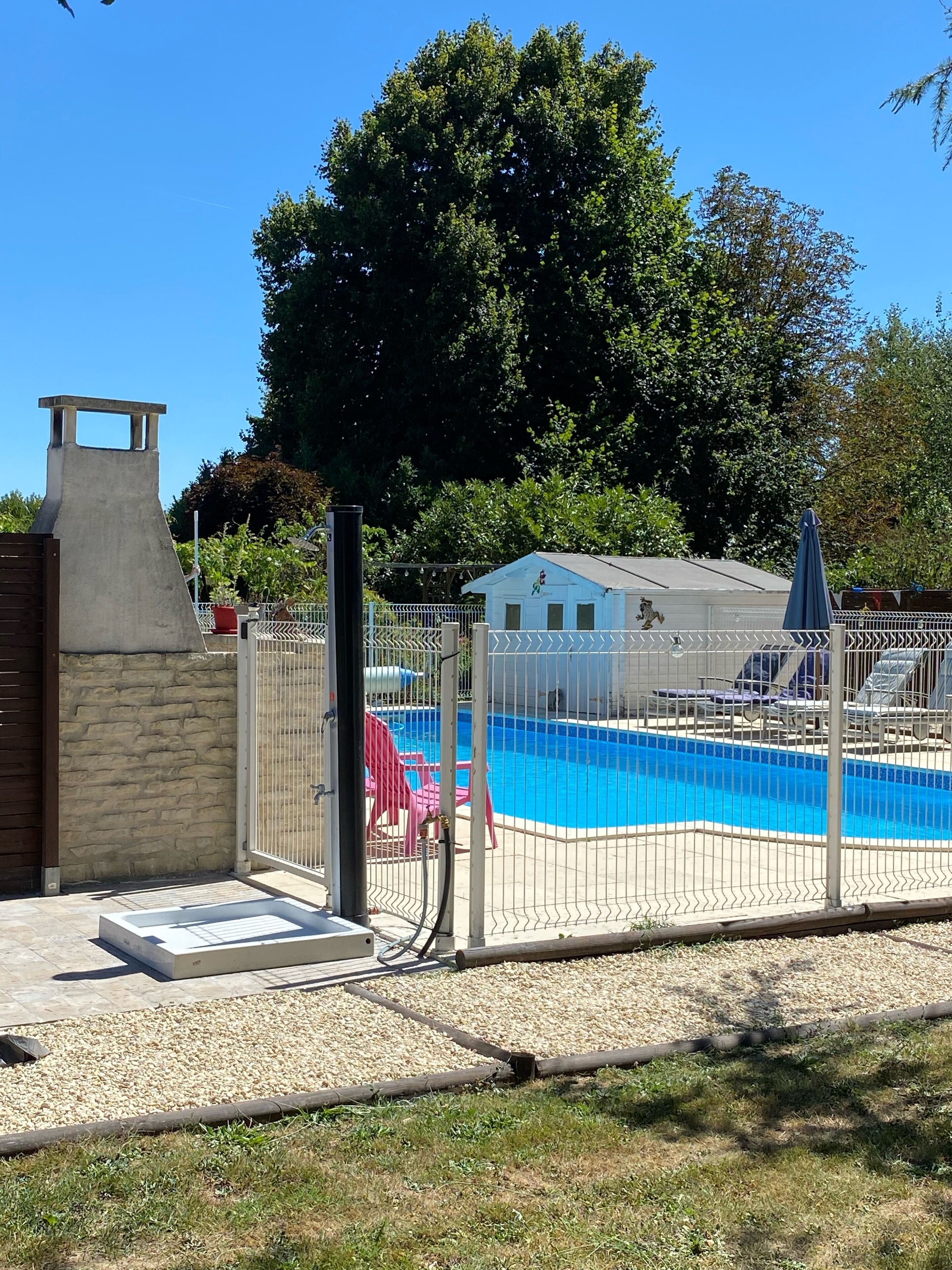 Una piscina rodeada por una valla, con un muro de piedra y una caseta pequeña al fondo.