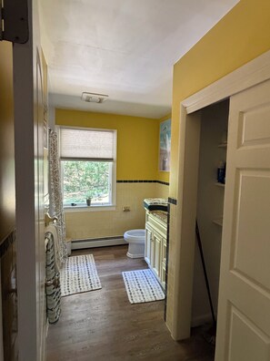 A bathroom with a toilet, a window, a radiator, and a door. - Overlook Ninigret Pond and Block Island (Charlestown)
